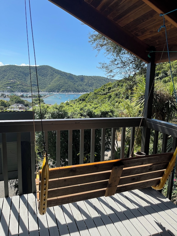 A wooden deck with a hammock, overlooking a coastal area with boats and greenery.