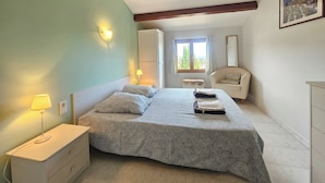 A bedroom with a bed, bedside table, lamp, wardrobe, window, chair, and a painting on the wall. - Charming villa with a pool and beautiful views (Montouliers)