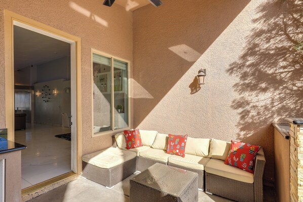 A sunlit patio with a wicker sofa, a small table, and a glass door leading to an interior space.