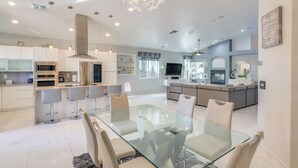 A modern kitchen with stainless steel appliances, a dining area with a glass table, and a living space with a large TV and seating area. - 12 Mi to the Strip: Las Vegas Home w/ Luxe Oasis! (Las Vegas)