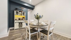 Un comedor con una mesa redonda, sillas blancas y un florero con flores.
