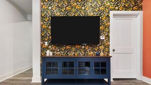 Una habitación con un armario azul oscuro, un televisor de pantalla plana montado sobre un papel tapiz floral y una puerta blanca.