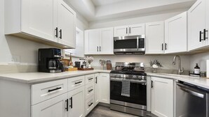Una cocina moderna con armarios blancos, estufa de acero inoxidable, microondas y lavavajillas.