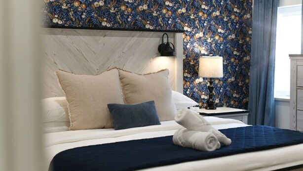 Una cama bien hecha con un edredón azul oscuro, dos almohadas y una toalla doblada.