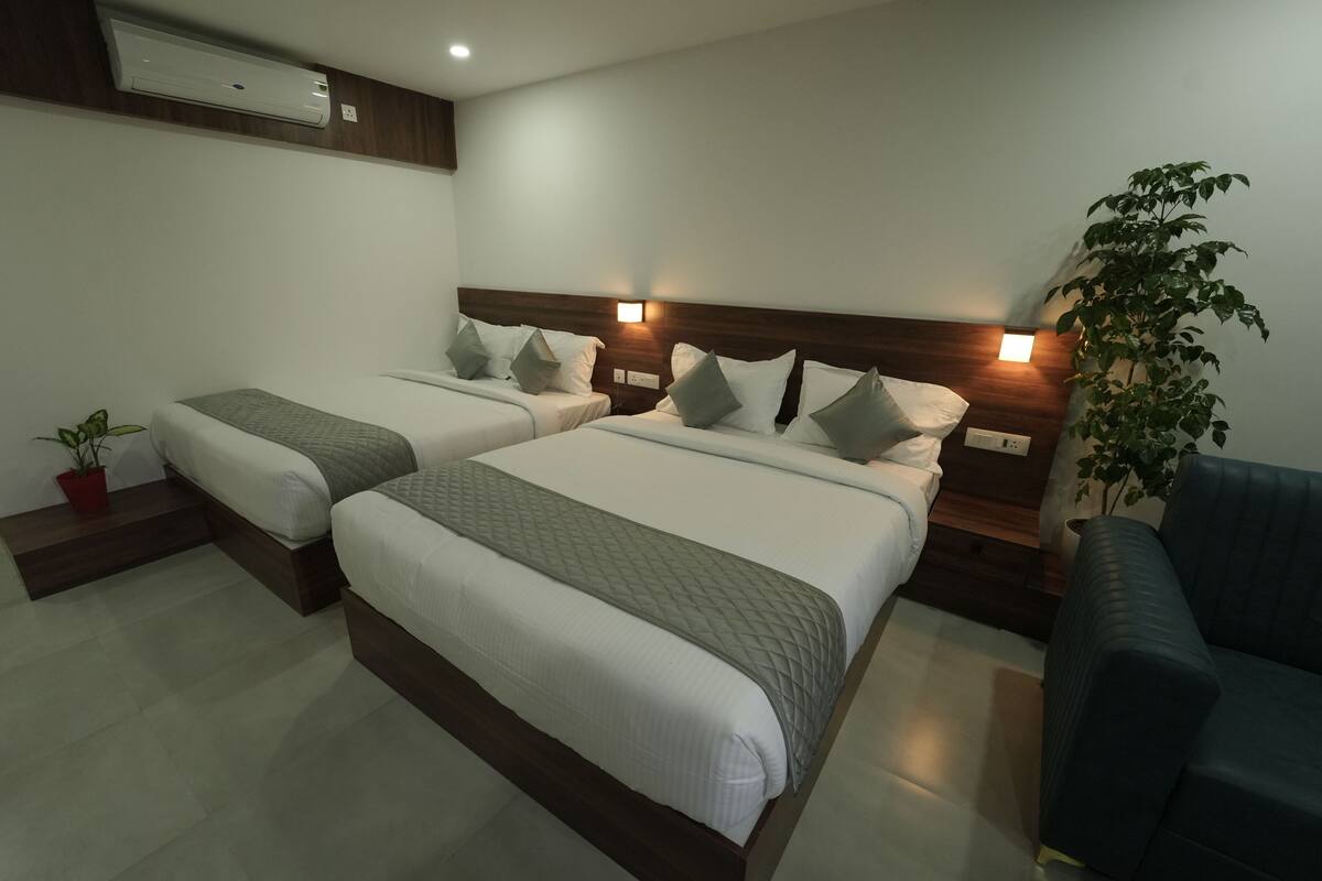 Une chambre d’hôtel avec deux lits, un canapé, une plante en pot et un appareil de climatisation.