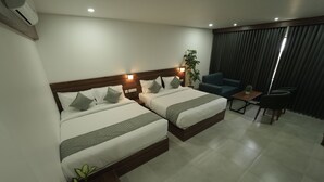 Een hotelkamer met twee bedden, een tafeltje, een stoel en een plant in pot.