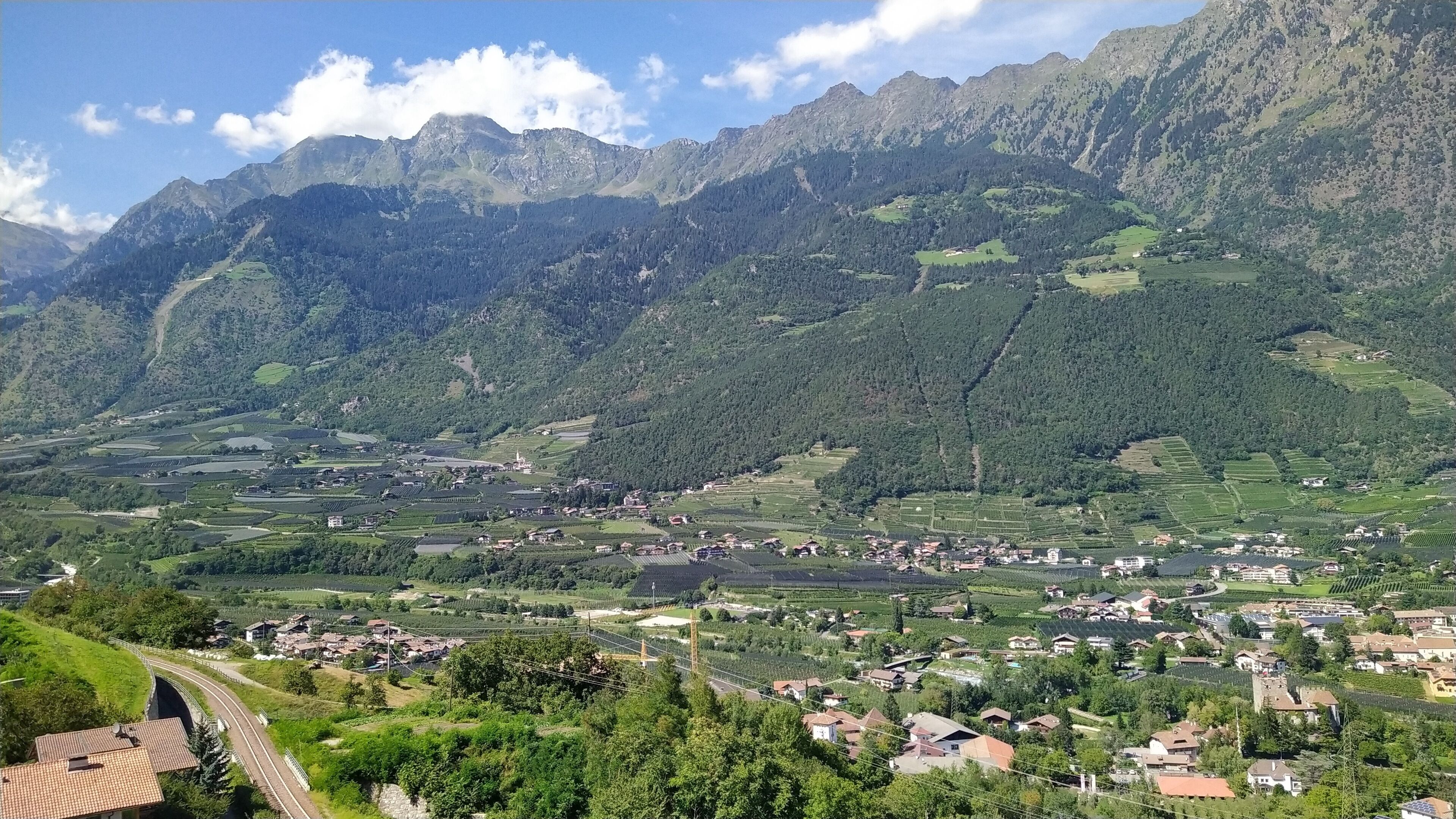 Un paysage montagneux avec une vallée, des maisons et une route sinueuse.
