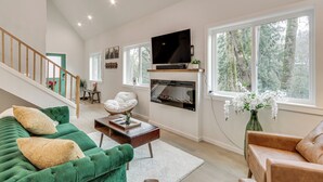 A spacious living room with a green sofa, a brown leather chair, a fireplace, and a television mounted on the wall. - Near Rivers & Boating: Home w/ Hot Tub in Longview (Longview)