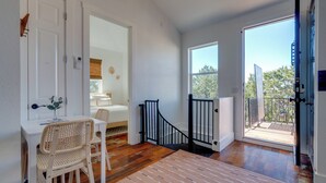 A room with a white desk, wicker chair, and a view of the outdoors through a large window. - Stylish Apt Near Lake Travis w/ Entertainment (Austin)