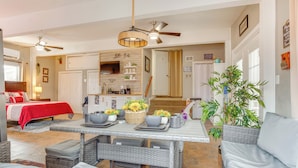 A spacious living area with a dining table, wicker furniture, and a red bed in the background. - 10 Mi to Dtwn Kansas City: Cozy Studio w/ Grill! (Kansas City)