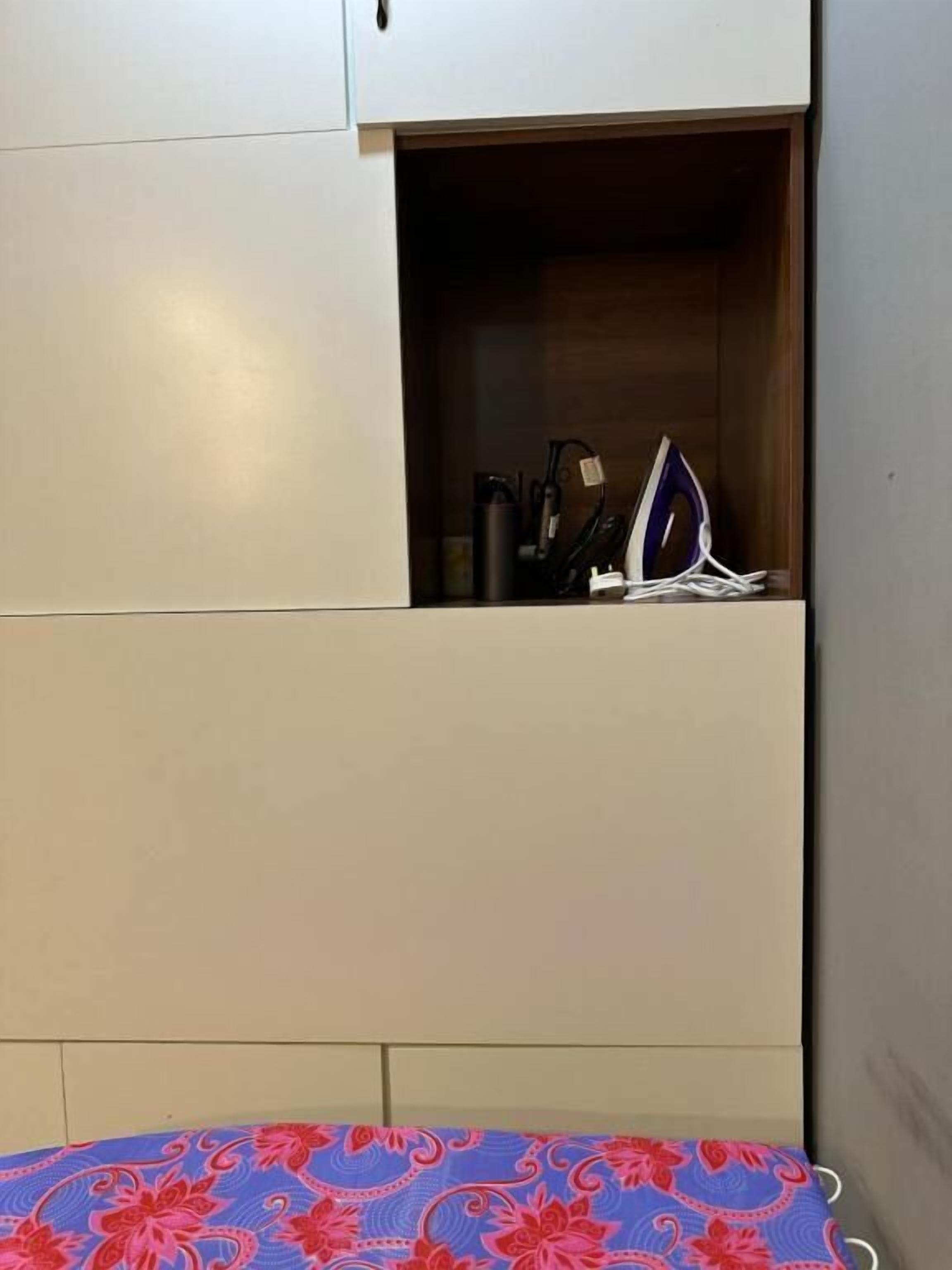 A bedroom with a bed, a wardrobe, and a small shelf with an iron and other items.