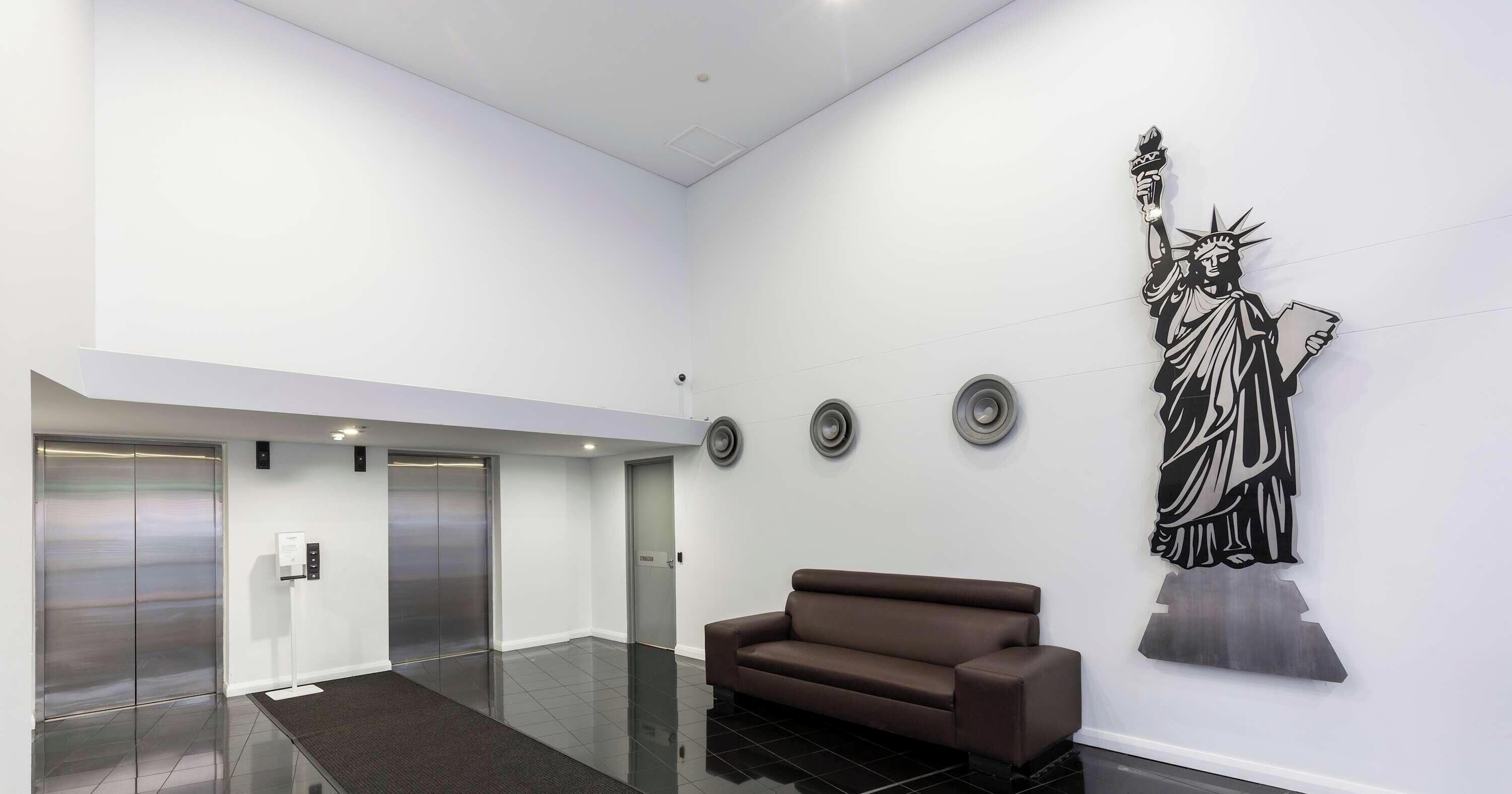 Un hall d’entrée avec un canapé marron, une statue et trois ascenseurs.
