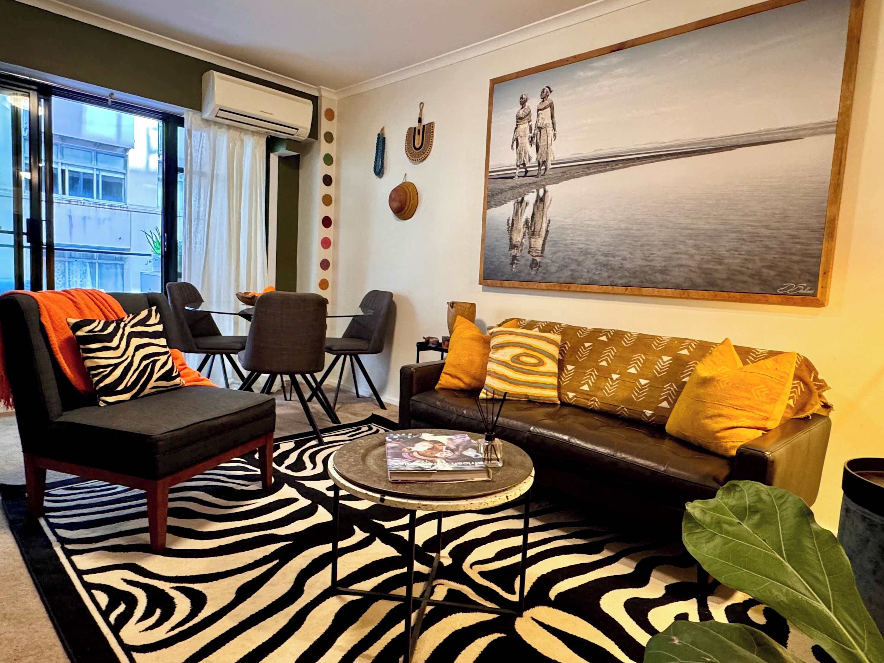 Un salon avec un tapis à motifs zébrés, un canapé agrémenté de coussins à motifs, une table basse et un tableau accroché au mur.