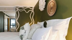 A bed with white linens and decorative pillows, a woven wall hanging, and a view of a balcony.