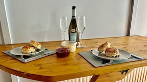 Une table en bois sur laquelle sont posées deux assiettes de scones, une bouteille de vin, deux verres et un pot de confiture.