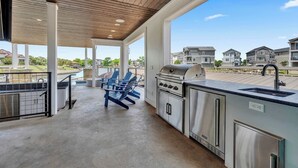 Un espace cuisine extérieur abrité, équipé d’un barbecue, de sièges et offrant une vue sur les maisons voisines.