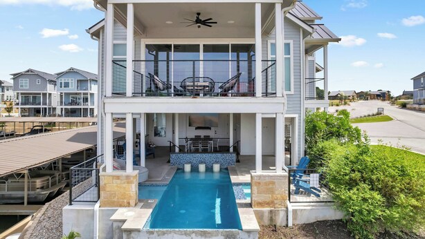 Une maison à deux étages avec une piscine, un espace salon extérieur et un balcon.