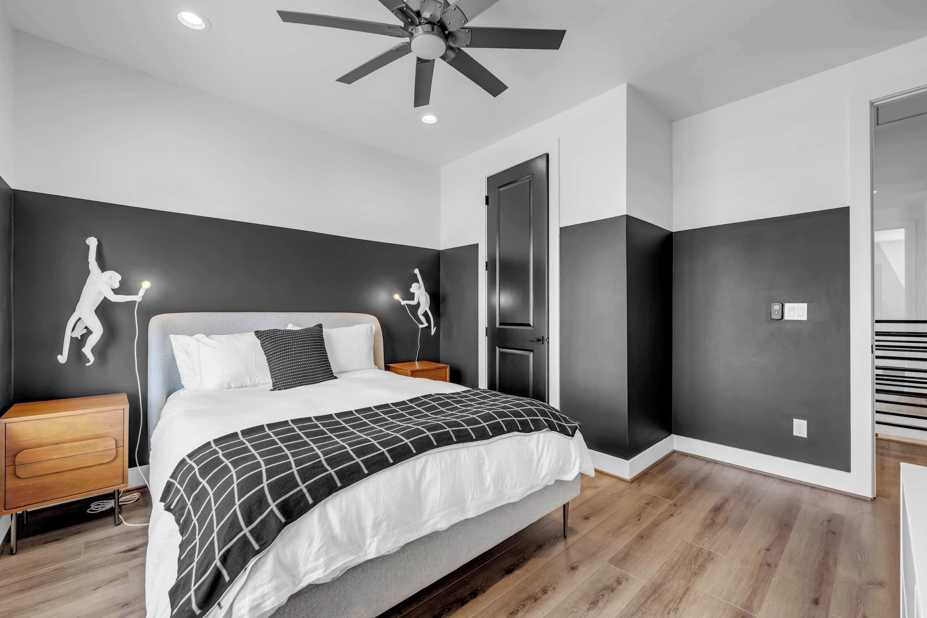 Quarto moderno com cama, ventoinha no teto, mesa de cabeceira e porta.