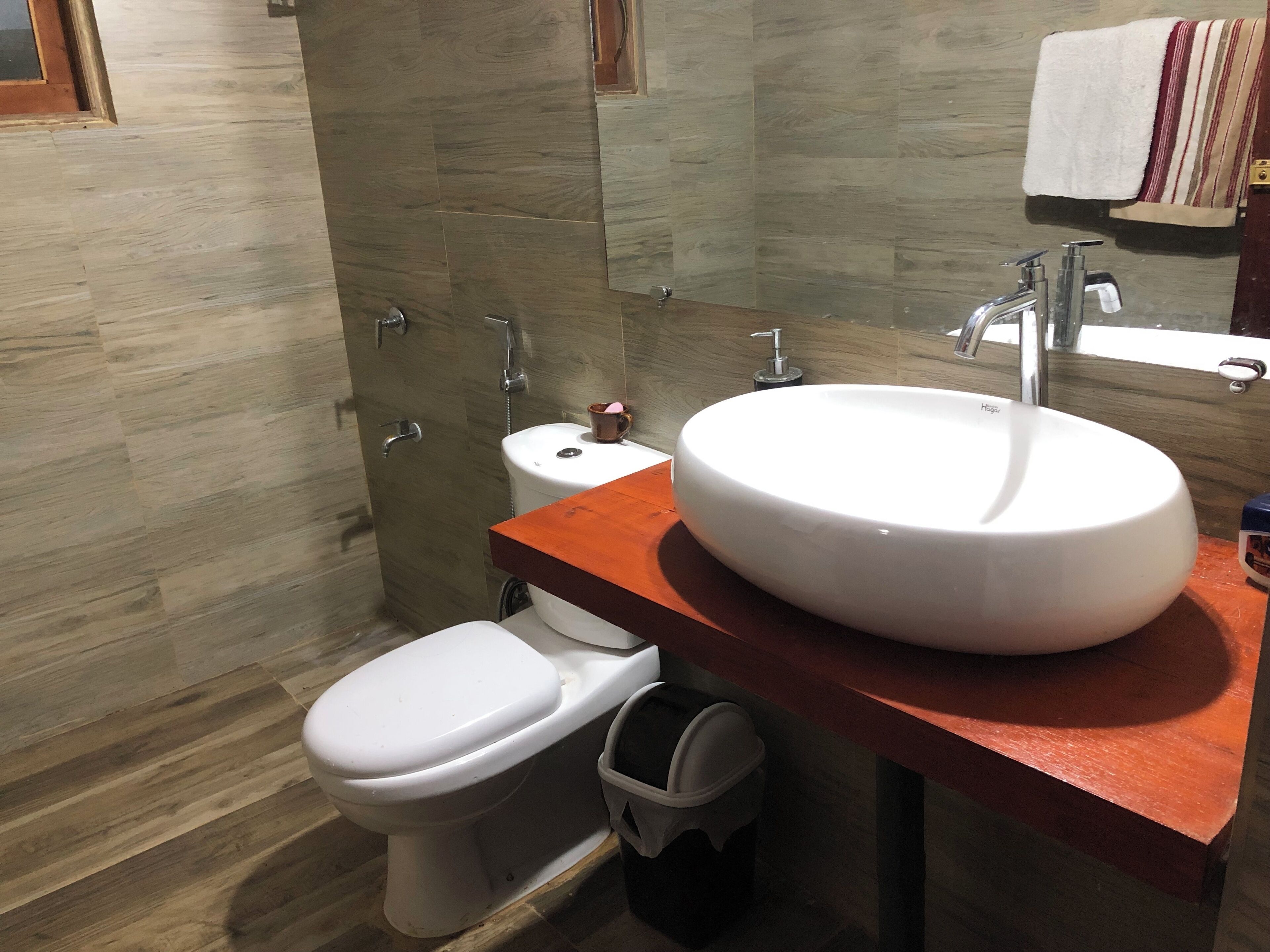 Un baño moderno con suelo de madera, inodoro blanco, un lavabo grande de color blanco y un espejo sobre el lavabo.