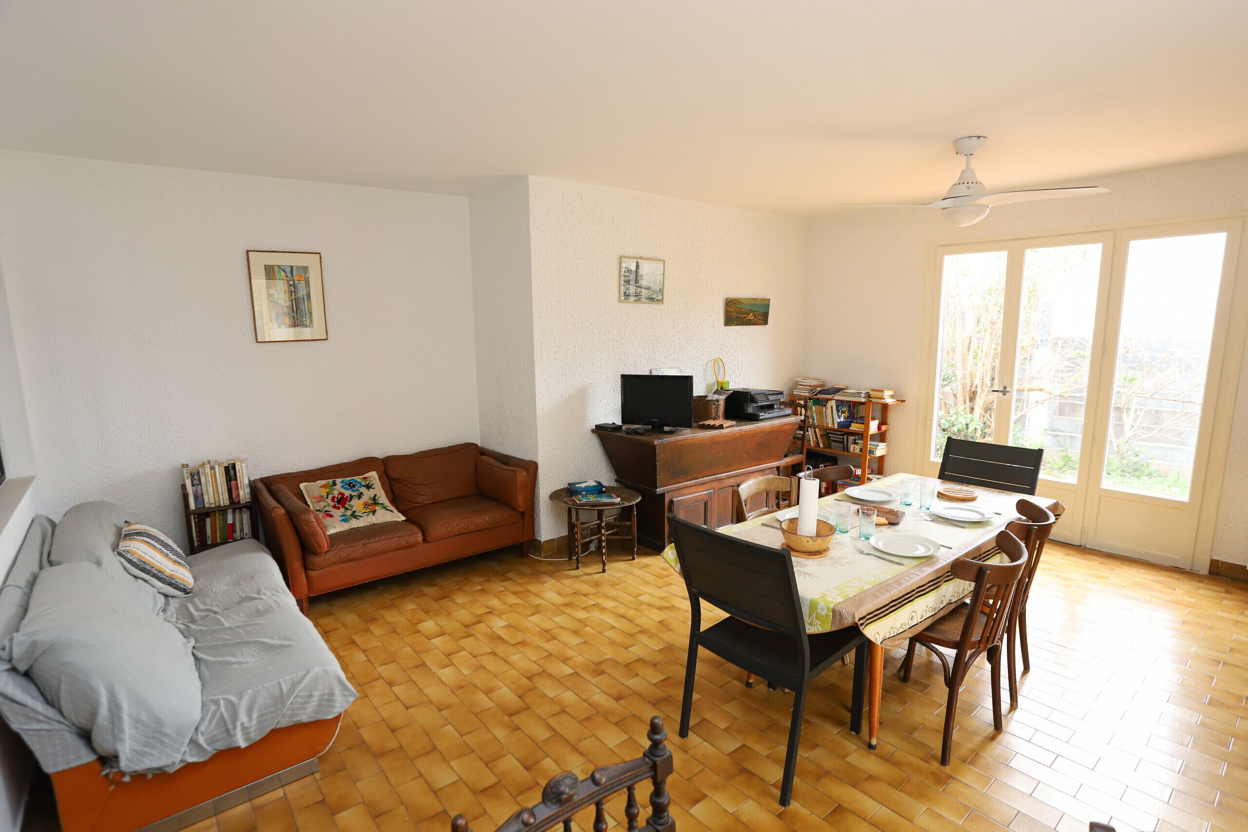 A living room with a sofa, a dining table with chairs, a TV, and a bookshelf.