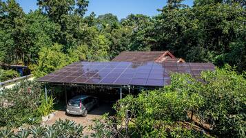 A house with a solar panel roof, a covered carport, and lush surrounding vegetation.