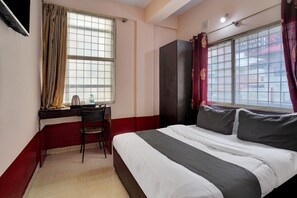 A hotel room with a bed, a desk, a chair, and a window with curtains.