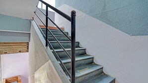 Un escalier avec une rampe noire et des marches en bois, menant à un palier sur lequel se trouve un coffre à motifs zébrés.
