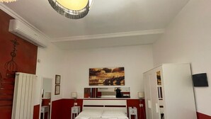 A hotel room with a bed, bedside tables, a mirror, a painting on the wall, and a wardrobe. - Family Suite (Roma)