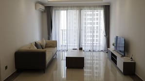 A modern living room with a sofa, a coffee table, a TV, and a window with sheer curtains. - R&F Hotel and Apartment (Phnom Penh)