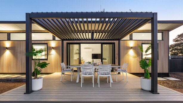 Ein moderner Essbereich im Freien mit einer Pergola, weißen Stühlen und Topfpflanzen.