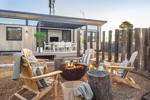 An outdoor seating area with Adirondack chairs, a fire pit, and a covered patio.