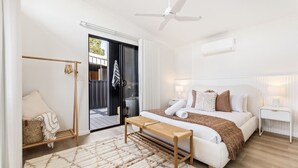 Ein modernes Schlafzimmer mit Bett, Nachttischen, einer Bank, einem Deckenventilator und einer Glastür, die zu einem Außenbereich führt.