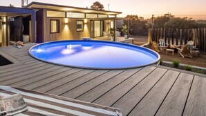 Ein modernes Haus mit Holzboden, einem Schwimmbad und Gartenmöbeln.