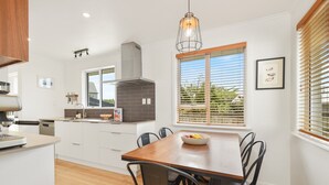 Una cocina moderna con armarios blancos, una mesa de comedor de madera y un ventanal con persianas.