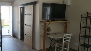 A small room with a television on a wooden stand, a table with a chair, and a door leading to an outdoor area. - Seasonal rental Oleron (Saint-Georges-d'Oléron)
