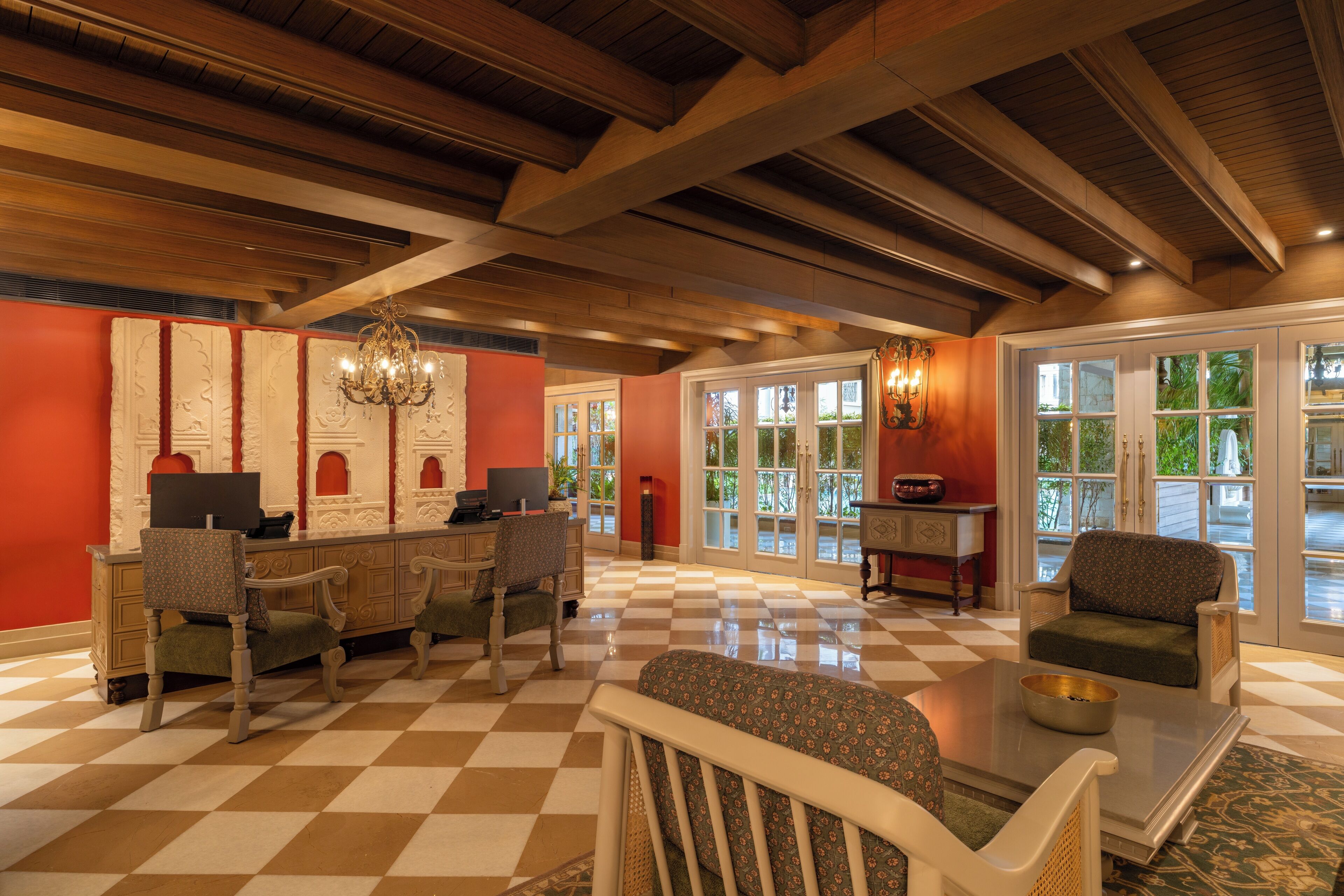 A lobby with checkered flooring, wooden beams, a chandelier, and seating areas with a view through large windows.