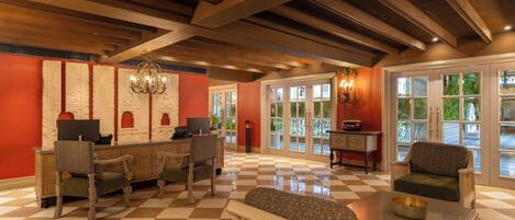 A lobby with checkered flooring, wooden beams, a chandelier, and seating areas with a view through large windows.