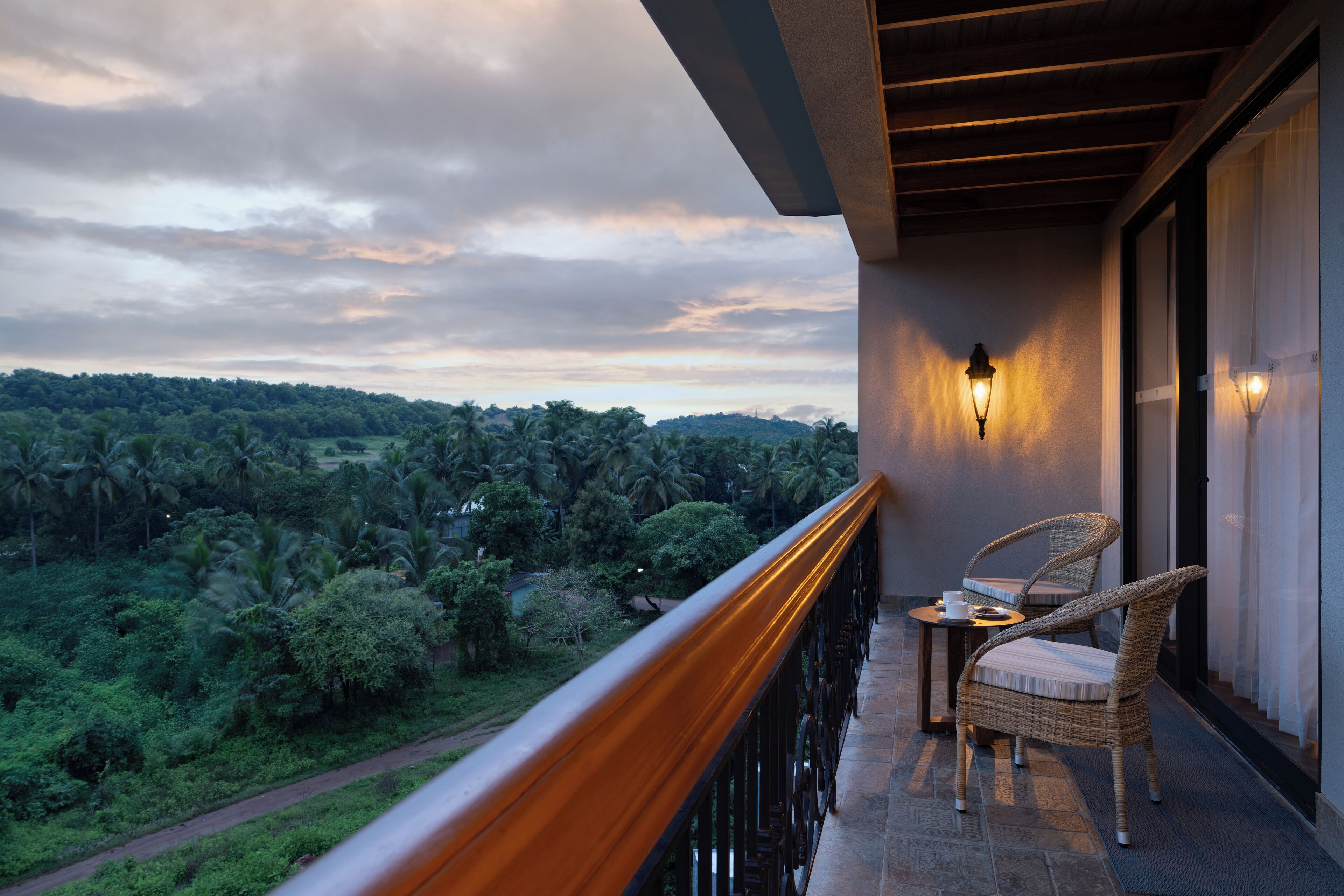 A balcony with a view of a lush landscape, a wicker chair, and a table with a cup.