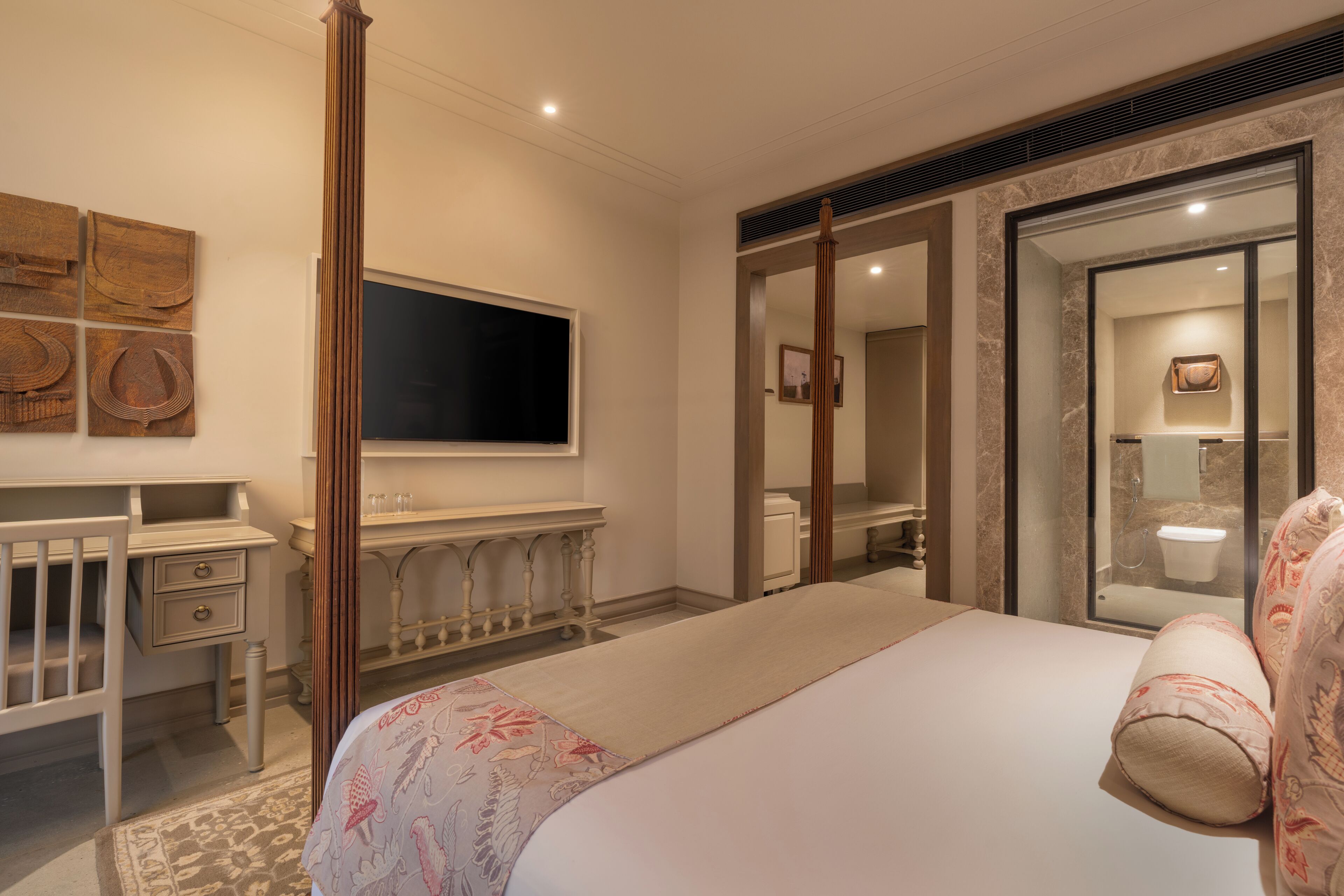 A hotel room with a large bed, a desk, a television, and a bathroom visible through a glass door.