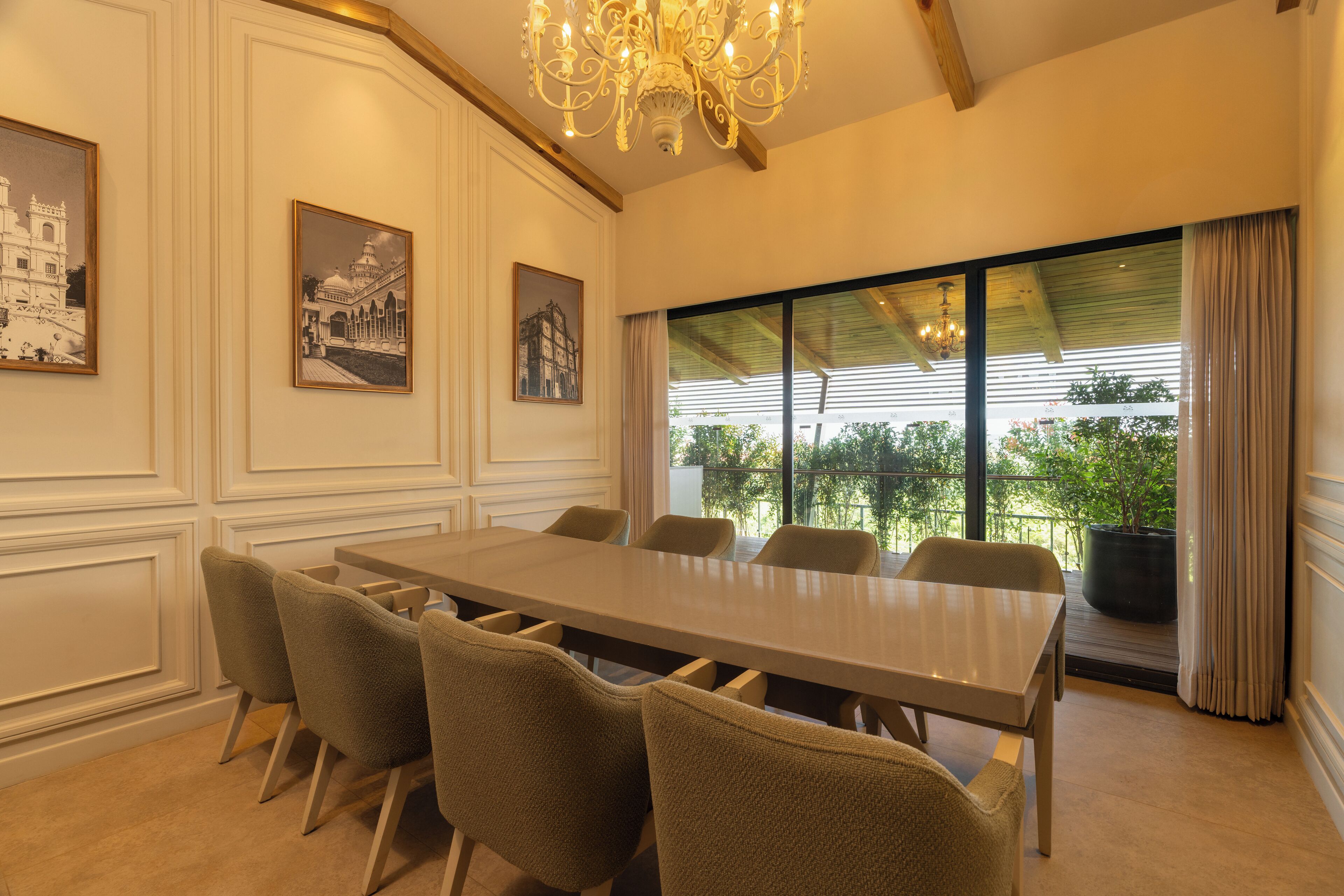 A conference room with a long table and six chairs, large windows with curtains, and framed pictures on the walls.