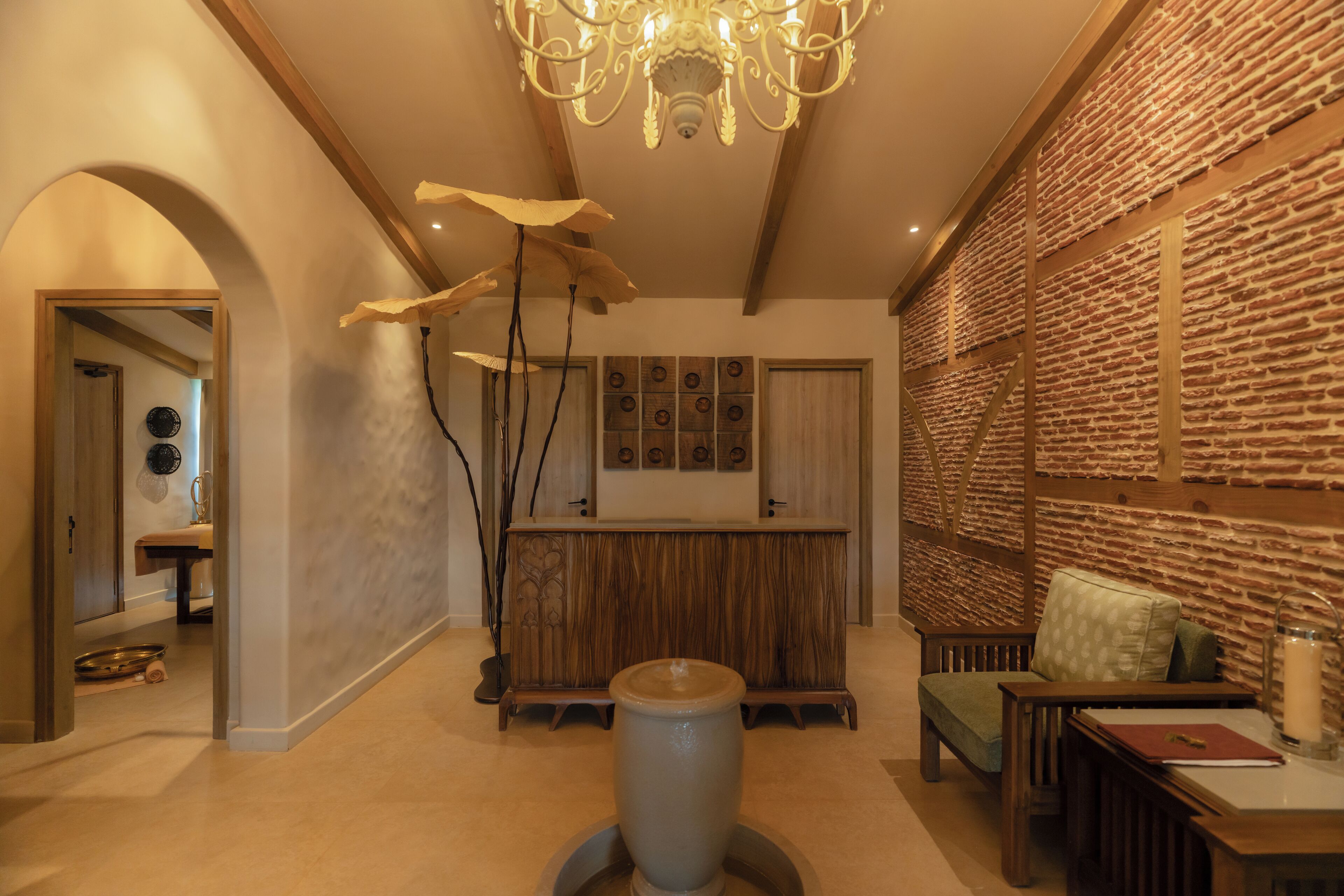 Un hall d’entrée spacieux avec un comptoir de réception en bois, un coin salon avec un banc rembourré, un grand vase et un lustre.