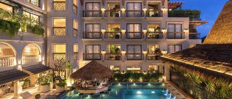 A hotel with a large swimming pool, outdoor seating, and multiple balconies with plants.