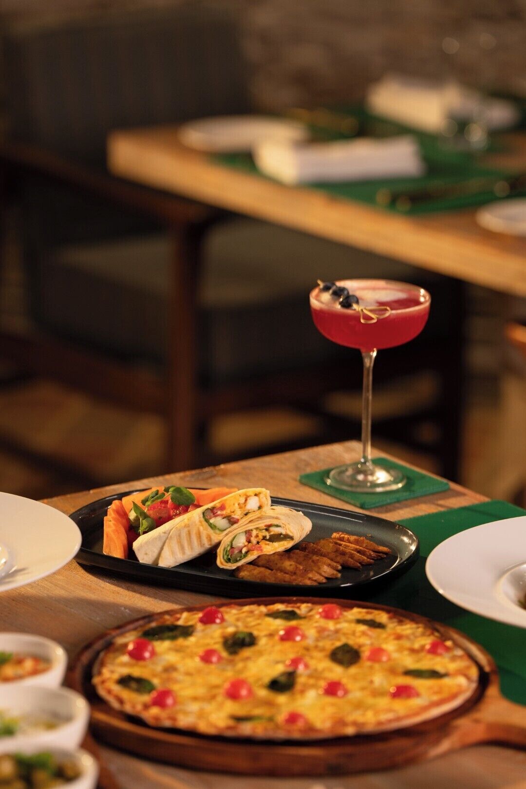 A dining table with a plate of food, a glass of red drink, and a pizza.