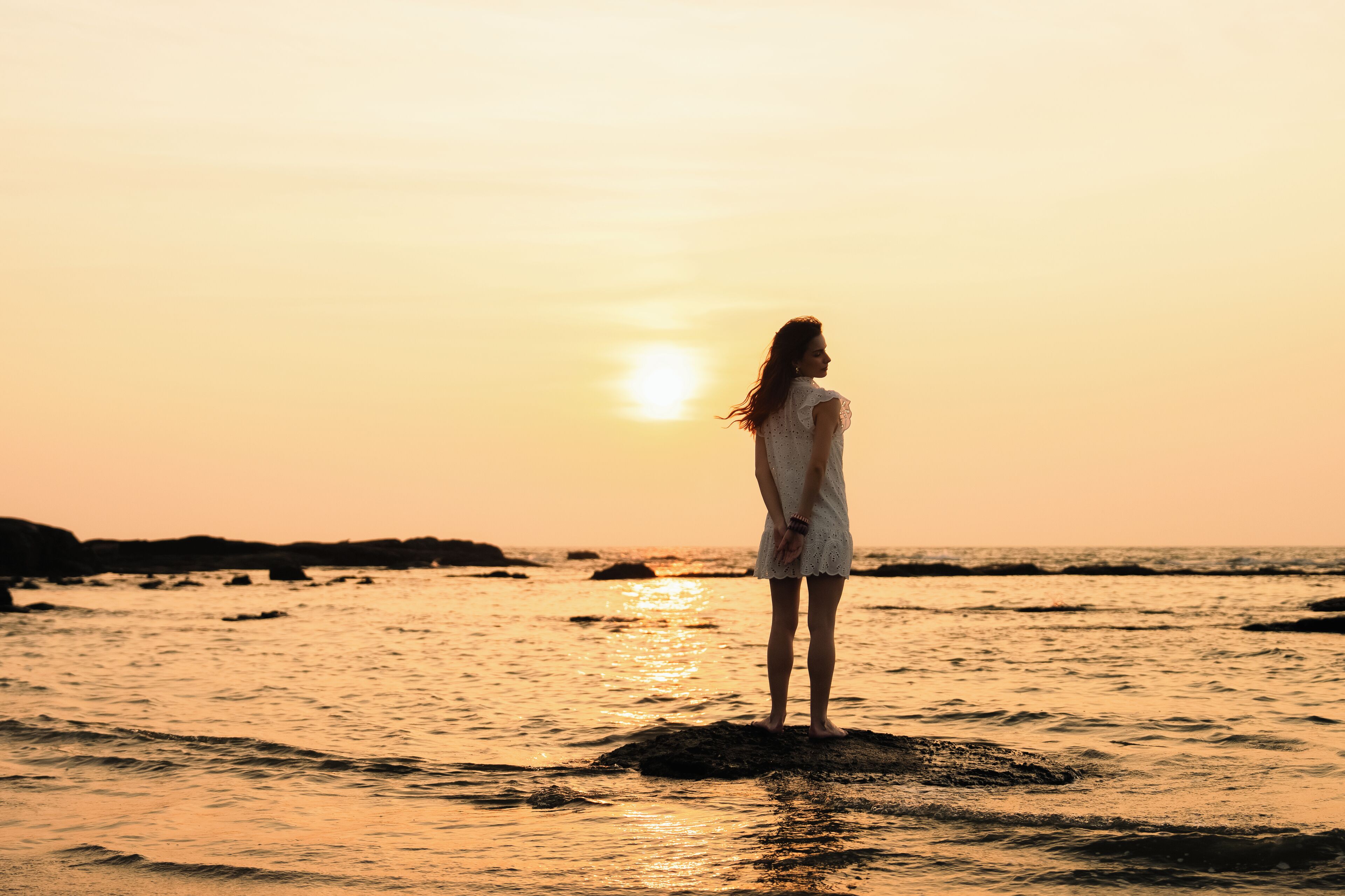 Une personne se tient debout sur un rocher, au bord de la mer, au coucher du soleil.