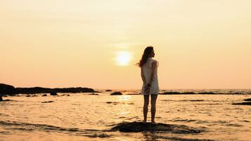 Une personne se tient debout sur un rocher, au bord de la mer, au coucher du soleil.