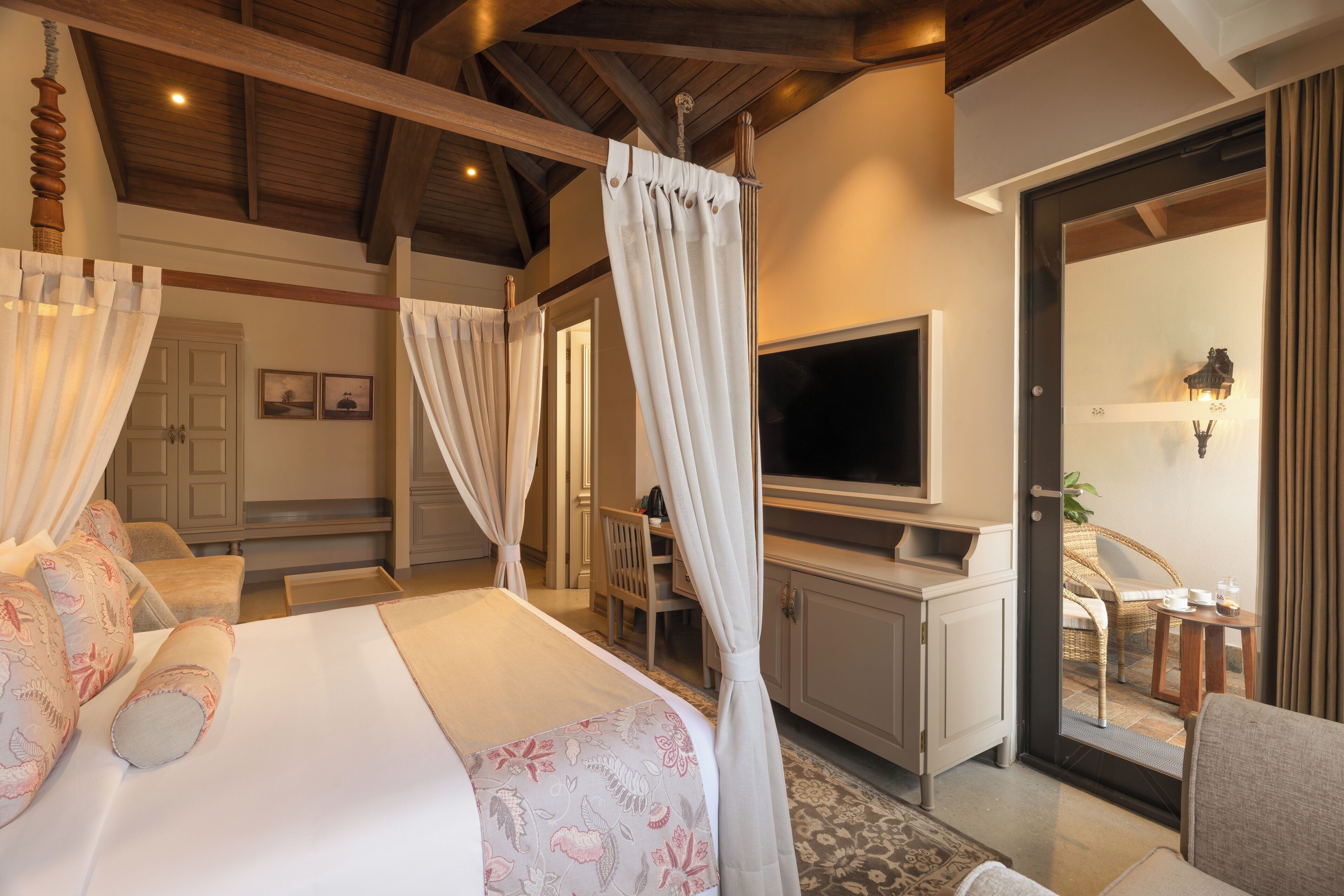 Une chambre à coucher avec un lit à baldaquin, une télévision et un balcon agrémenté de meubles en osier.