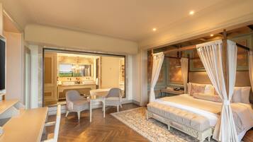 A bedroom with a four-poster bed, a sitting area with chairs, a desk, and a view of the bathroom.