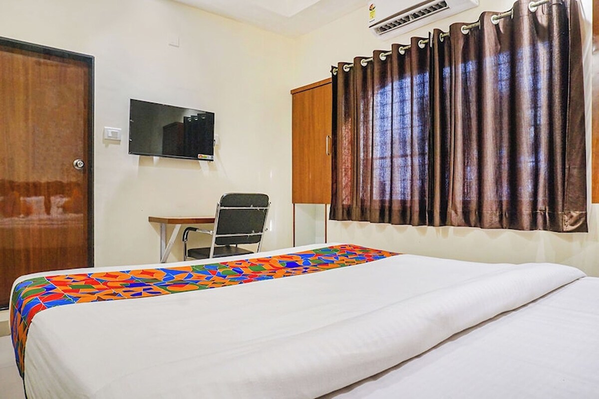 A hotel room with a bed, a desk, a chair, a TV, and curtains.