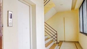 Una escalera de madera con barandillas de metal que conduce a un rellano con una puerta blanca y un dispositivo de seguridad en la pared.