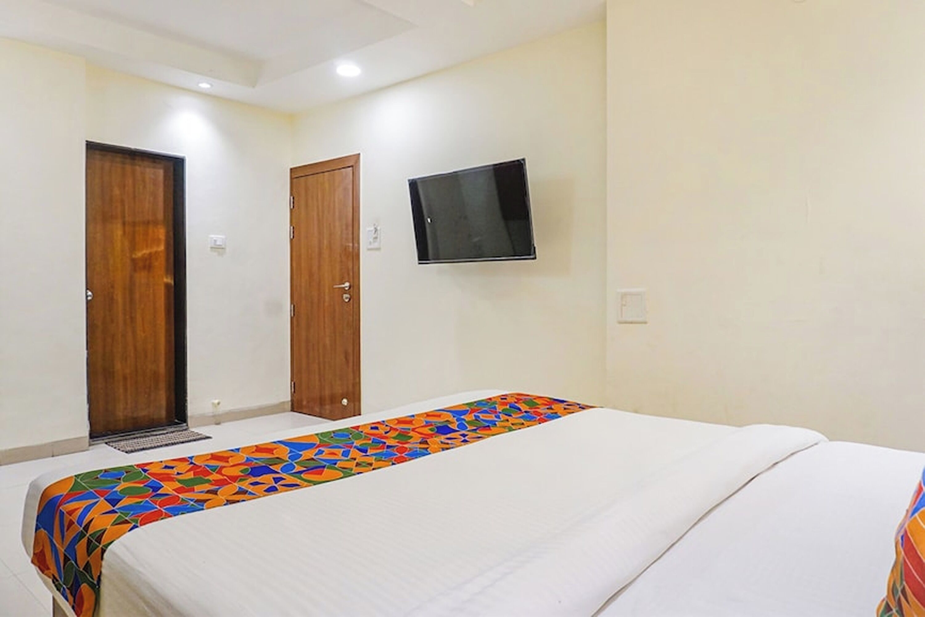 A hotel room with a bed, a TV mounted on the wall, and two wooden doors.